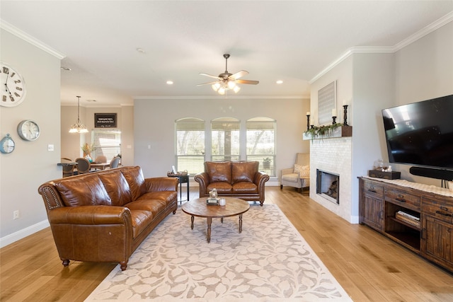 living room with a tiled fireplace, light wood-type flooring, ceiling fan with notable chandelier, and ornamental molding