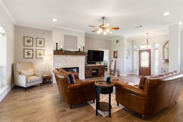 living room featuring a fireplace, light wood-type flooring, ceiling fan, and crown molding