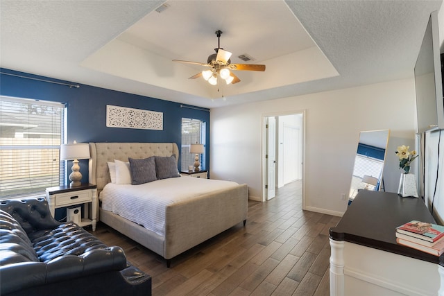 bedroom with ceiling fan, dark wood-type flooring, and a tray ceiling