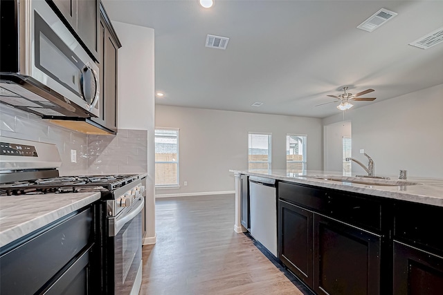 kitchen with light stone countertops, ceiling fan, sink, stainless steel appliances, and light wood-type flooring