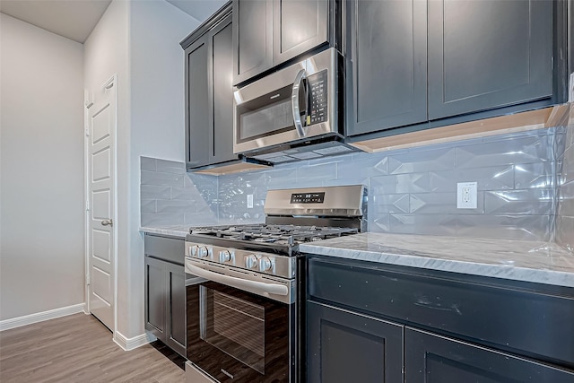 kitchen with decorative backsplash, light hardwood / wood-style flooring, light stone countertops, and appliances with stainless steel finishes