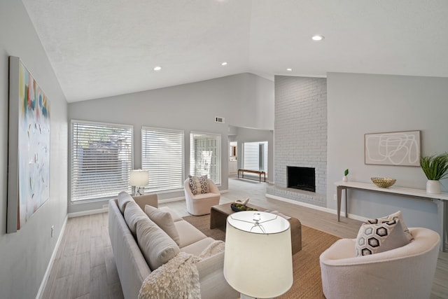 living room featuring light hardwood / wood-style flooring, high vaulted ceiling, and a brick fireplace