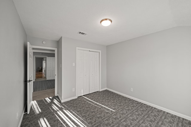 unfurnished bedroom with lofted ceiling, a closet, carpet, and a textured ceiling