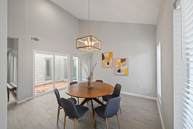 dining area with light hardwood / wood-style floors, high vaulted ceiling, and a notable chandelier