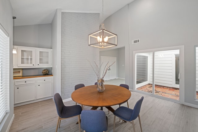 dining space with light wood-type flooring, an inviting chandelier, and high vaulted ceiling