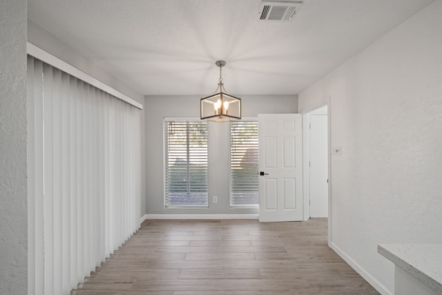 unfurnished dining area featuring light wood-type flooring, a textured ceiling, and a chandelier