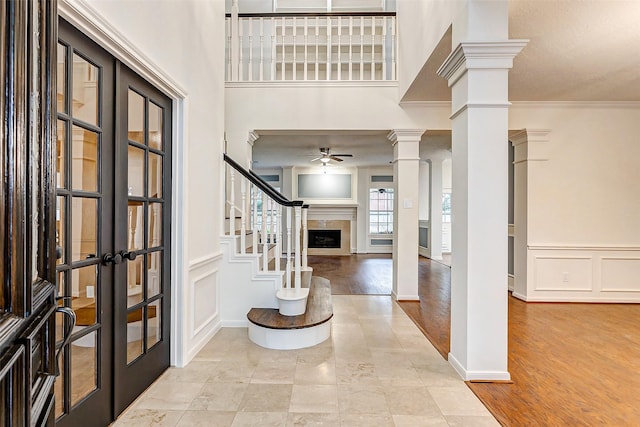 entrance foyer with a tile fireplace, ornate columns, crown molding, ceiling fan, and french doors