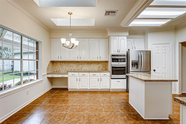 kitchen with appliances with stainless steel finishes, decorative light fixtures, backsplash, white cabinetry, and a skylight