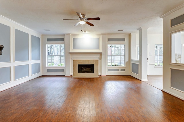 unfurnished living room with ceiling fan, hardwood / wood-style floors, a tile fireplace, and ornamental molding