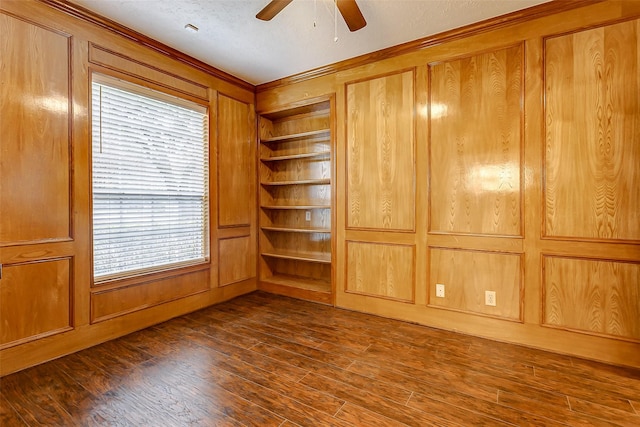 empty room featuring built in shelves, wood walls, plenty of natural light, and dark hardwood / wood-style flooring