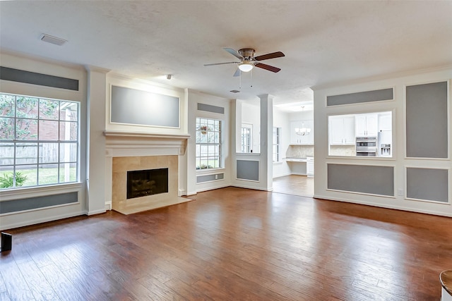 unfurnished living room featuring ceiling fan with notable chandelier, wood-type flooring, a healthy amount of sunlight, and a fireplace