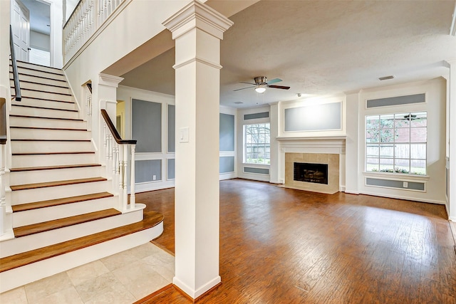 unfurnished living room with hardwood / wood-style floors, crown molding, decorative columns, a tile fireplace, and ceiling fan