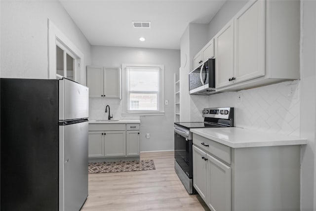 kitchen with white cabinetry, sink, stainless steel appliances, light hardwood / wood-style flooring, and backsplash