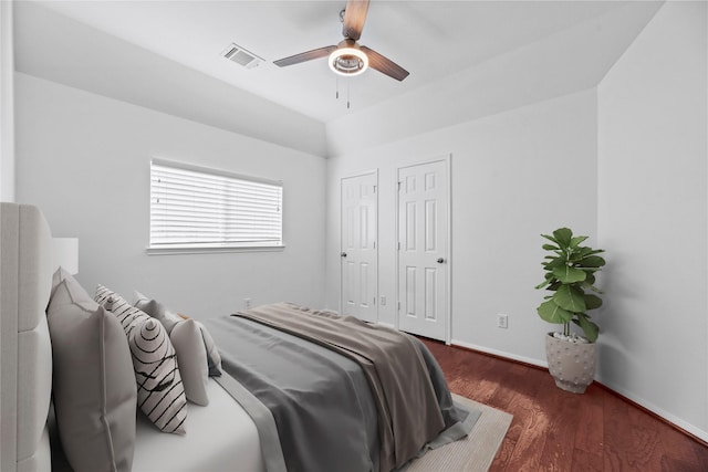 bedroom featuring two closets, dark wood-type flooring, ceiling fan, and vaulted ceiling