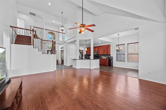 unfurnished living room with ceiling fan with notable chandelier, dark wood-type flooring, and high vaulted ceiling