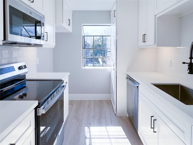 kitchen with tasteful backsplash, white cabinetry, sink, light hardwood / wood-style flooring, and stainless steel appliances