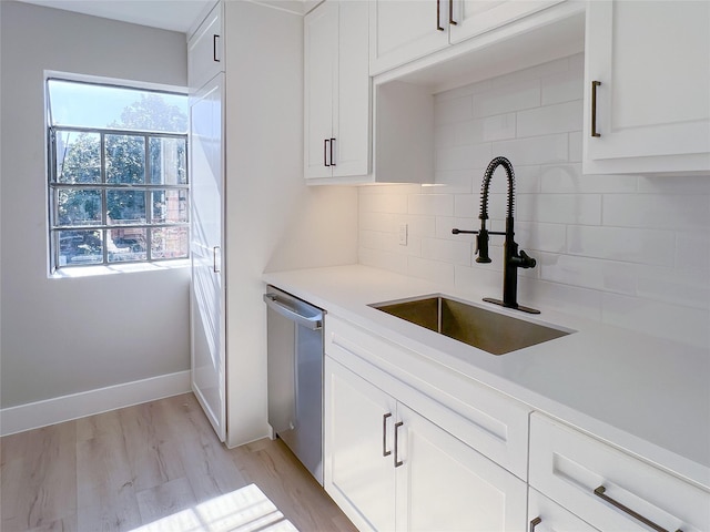 kitchen featuring backsplash, dishwasher, sink, white cabinetry, and light hardwood / wood-style flooring