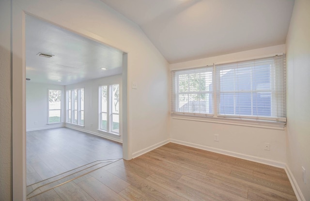 empty room featuring plenty of natural light, light hardwood / wood-style floors, and vaulted ceiling