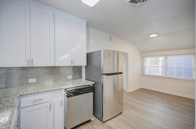 kitchen featuring light stone countertops, light wood-type flooring, stainless steel appliances, vaulted ceiling, and white cabinets