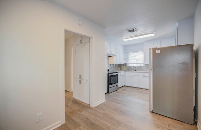 kitchen featuring appliances with stainless steel finishes, backsplash, sink, light hardwood / wood-style flooring, and white cabinetry