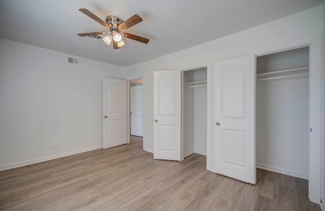 unfurnished bedroom with ceiling fan, light wood-type flooring, and two closets