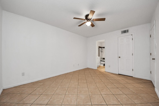 unfurnished bedroom featuring ceiling fan, ensuite bathroom, a textured ceiling, a closet, and light tile patterned floors