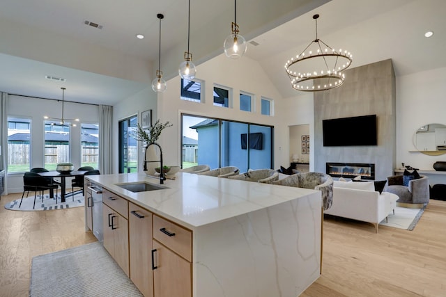 kitchen with a center island with sink, sink, a fireplace, decorative light fixtures, and light stone counters