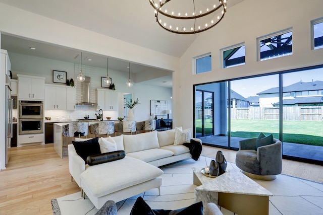 living room featuring high vaulted ceiling, light hardwood / wood-style floors, and an inviting chandelier