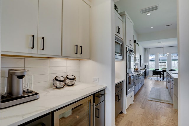 kitchen with white cabinetry, light stone countertops, hanging light fixtures, wine cooler, and light wood-type flooring