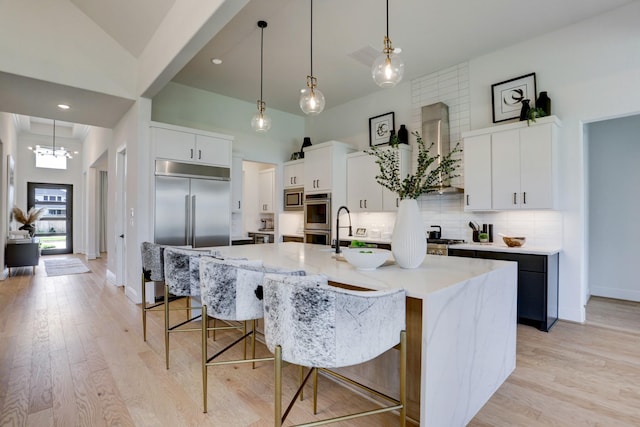 kitchen featuring built in appliances, decorative light fixtures, white cabinetry, and a large island