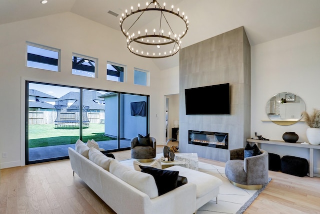 living room with a large fireplace, light hardwood / wood-style floors, high vaulted ceiling, and a notable chandelier