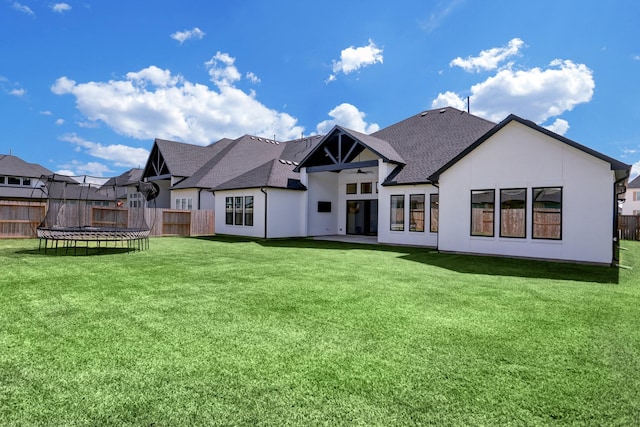 rear view of property featuring a yard and a trampoline