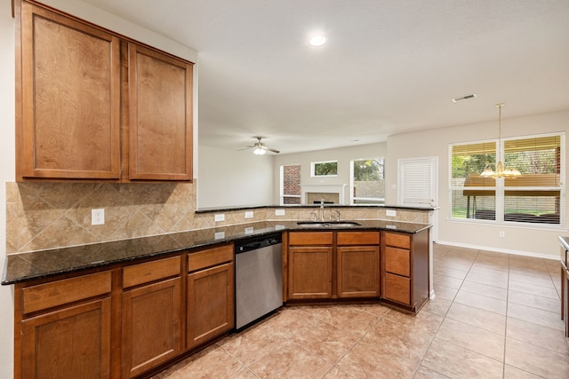 kitchen featuring stainless steel dishwasher, ceiling fan with notable chandelier, sink, pendant lighting, and dark stone countertops