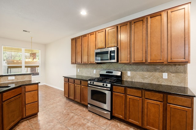 kitchen with stainless steel appliances, dark stone countertops, pendant lighting, decorative backsplash, and light tile patterned floors