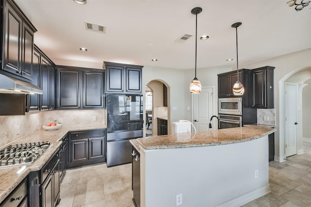 kitchen with a kitchen island with sink, light stone counters, pendant lighting, decorative backsplash, and appliances with stainless steel finishes