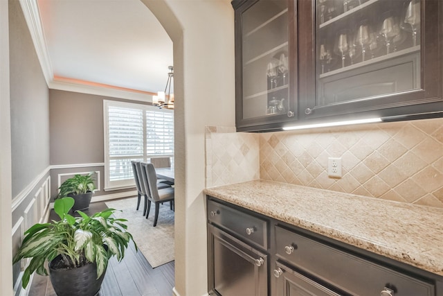 kitchen featuring light stone countertops, ornamental molding, dark brown cabinets, wood-type flooring, and a chandelier