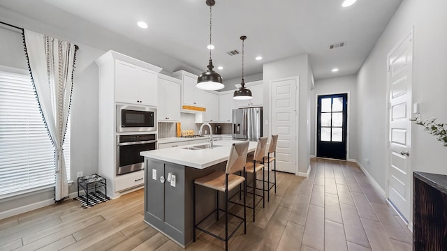 kitchen featuring hanging light fixtures, stainless steel appliances, a kitchen bar, a kitchen island with sink, and white cabinetry