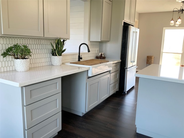 kitchen with dark wood-style floors, pendant lighting, high end fridge, backsplash, and a sink