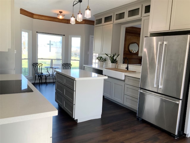 kitchen featuring dark wood-type flooring, hanging light fixtures, black electric cooktop, a kitchen island, and stainless steel refrigerator