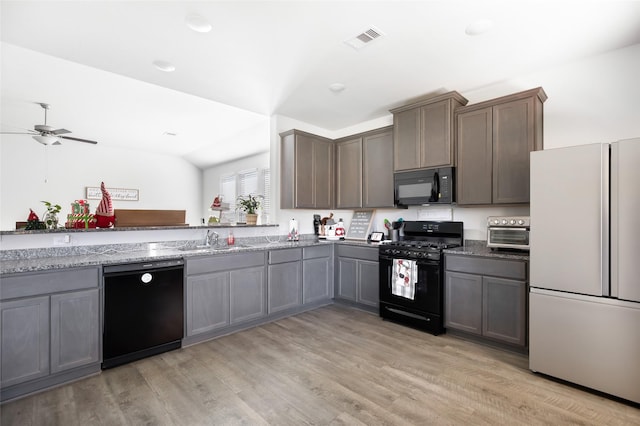 kitchen with light wood-type flooring, sink, black appliances, dark stone countertops, and lofted ceiling