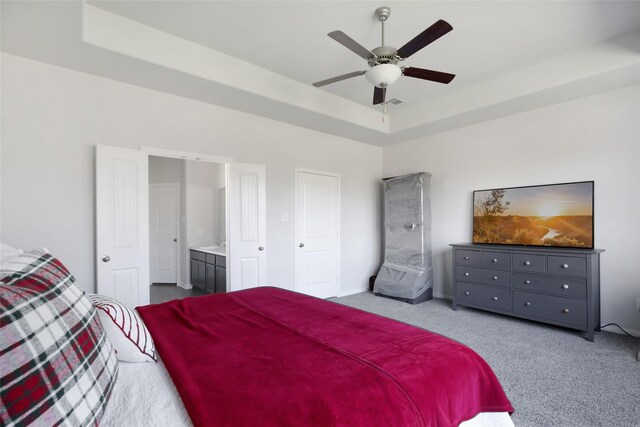 carpeted bedroom featuring a tray ceiling, ensuite bath, and ceiling fan