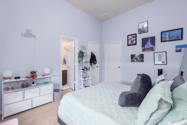 bedroom with ensuite bathroom, light colored carpet, and a towering ceiling