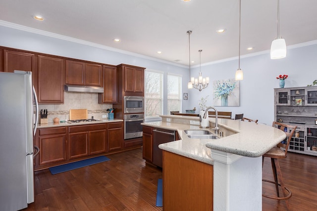 kitchen with decorative light fixtures, stainless steel appliances, a kitchen island with sink, and sink