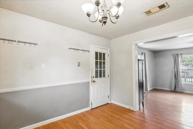 unfurnished room featuring hardwood / wood-style floors, a textured ceiling, and an inviting chandelier