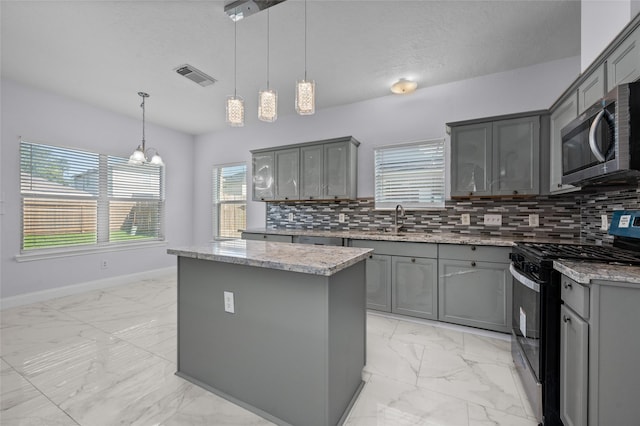 kitchen featuring tasteful backsplash, stainless steel appliances, decorative light fixtures, gray cabinets, and a kitchen island