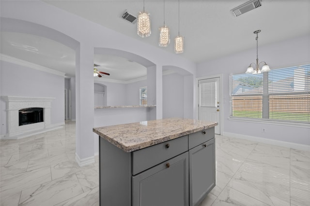 kitchen with a center island, ceiling fan with notable chandelier, hanging light fixtures, gray cabinets, and light stone countertops