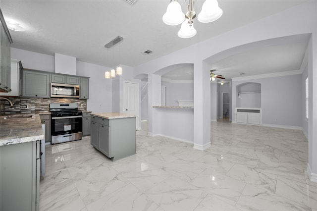 kitchen featuring gray cabinetry, pendant lighting, ceiling fan with notable chandelier, a kitchen island, and stainless steel appliances