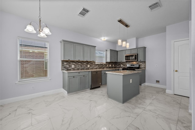 kitchen featuring gray cabinetry, hanging light fixtures, a chandelier, a kitchen island, and appliances with stainless steel finishes