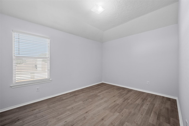 spare room featuring a textured ceiling, dark wood-type flooring, and lofted ceiling