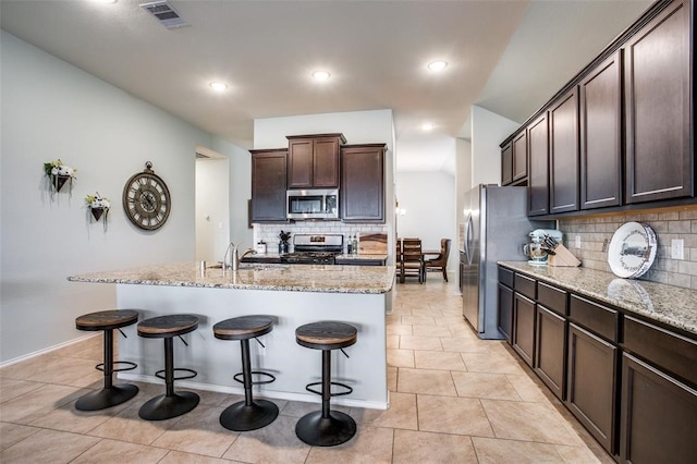 kitchen featuring tasteful backsplash, a breakfast bar, an island with sink, and appliances with stainless steel finishes